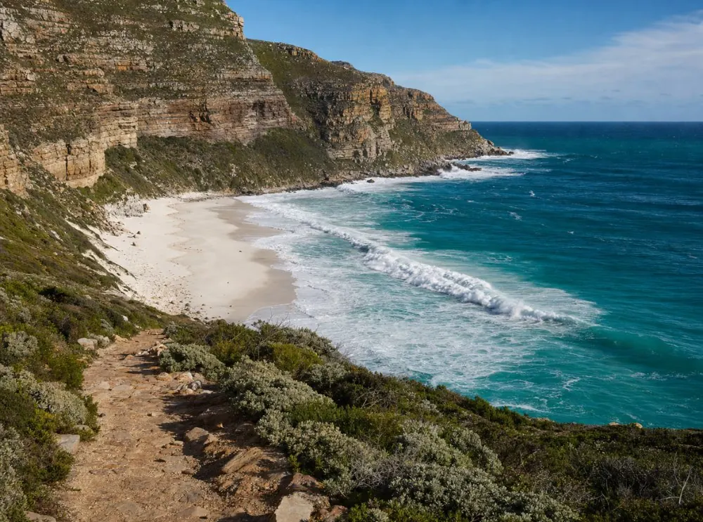 A white sand beach below high cliffs with rolling surf on the Cape Peninsula