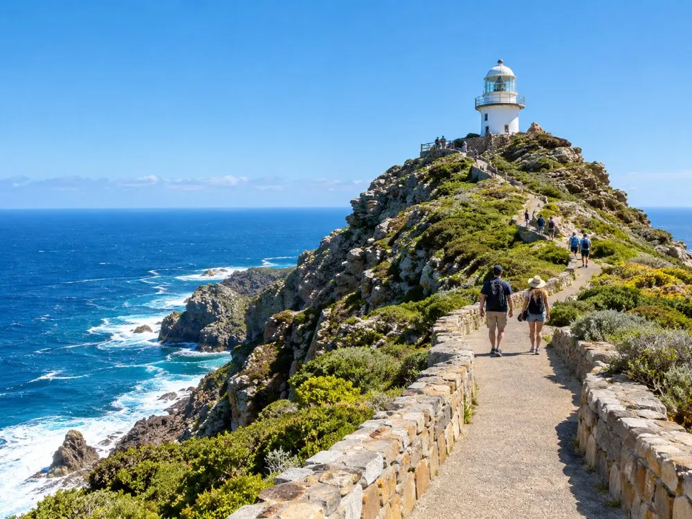 A paved path with low stone walls climbing to the old white lighthouse at Cape Point